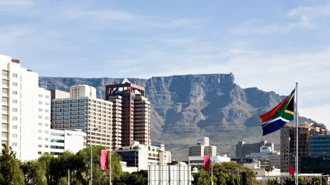 Table Mountain rises behind downtown Cape Town, with the South African flag flies at right.