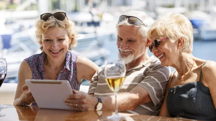 Senior friends smiling and using a digital tablet on a yacht.