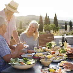 A group of mature friends are sitting around an outdoor dining table in Tuscany, Italy