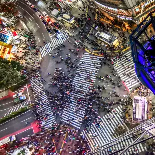 Aerial view of busy Shibuya crossing in Tokyo in-between large skyscrapers adorned with advertising screens, Japan