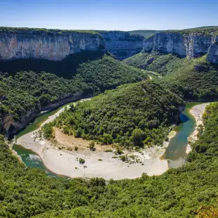 Curving Ardeche River, surrounded by tall trees and a cliff, France