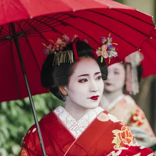 Beautiful Maiko with red clothing and umbrella in the streets of Kyoto, Japan