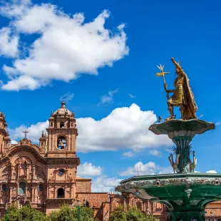 A golden fountain and an impressive religious building in Cuzco Main Square, Peru