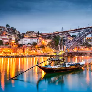 Rabelo boats on the Douro River and Porto skyline illuminated at night in Portugal