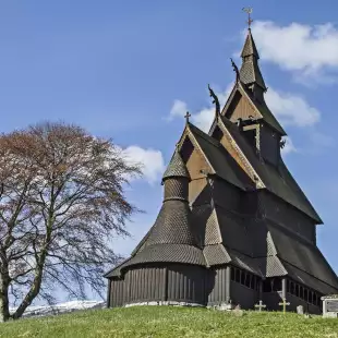 Preserved wooden Hopperstad Stave Church besides a tree atop a green hill, Norway