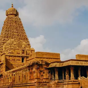 Hindu Temple showcasing Chola architectural style, built with a pyramid shaped spire. Stone steps lead to the entrance hidden under a column-supported roof