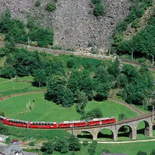 A red train in motion curved along the Brusio Spiral Viaduct on the Bernina Railway