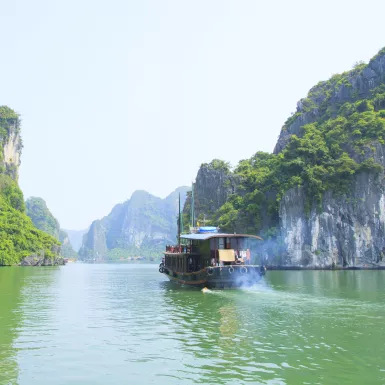 A river boat moving across the turquoise waters of Halong Bay 