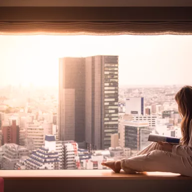 A woman in her pyjamas, looking out of her hotel window at the cityscape of Shibuya, Tokyo. 