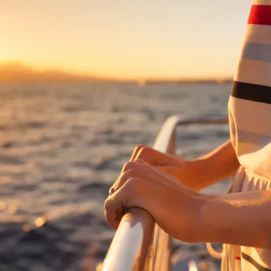 Close-up of hands holding onto rail on a yacht during sunset