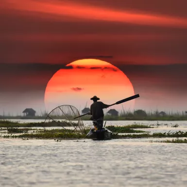 Vietnamese fisherman on his boat during sunset, balancing a oar paddle