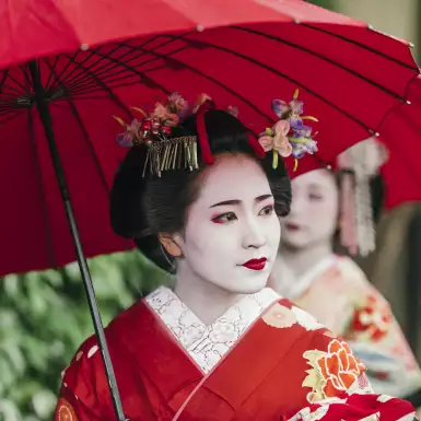 Beautiful Maiko with red clothing and umbrella in the streets of Kyoto, Japan