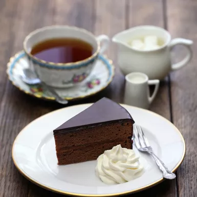 Homemade sachertorte, Austrian chocolate cake with a dollop of whipped cream and some tea 