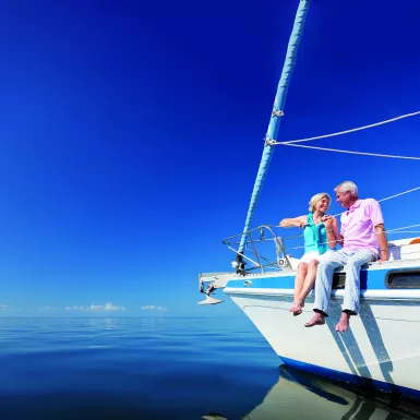 Happy senior couple sitting on the bow of a sail boat on a calm blue sea