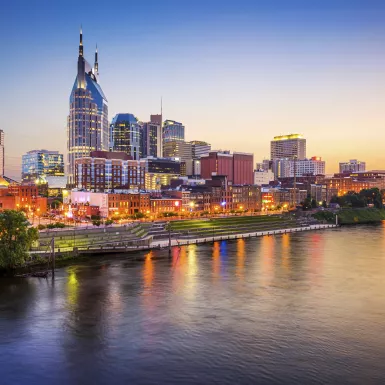 Nashville downtown skyline before sunset along a clear sky, it's reflection displayed in the foreground of the Cumberland River.