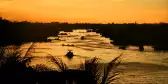 Sunset skies over Mekong River with silhouettes of tree and boats visible along the water