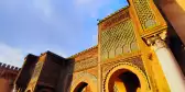 Bab El Mansour Laalej, an ornate monumental gate in the city of Meknes featuring stone archways and lattice-like patterns above stone columns 