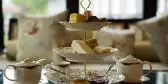 Three tier cake stand set up for an afternoon tea with cakes and servings of jam, plus two teapots