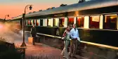 Mature couple walking on platform beside the Pride of Africa train and a man carrying luggage