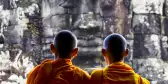 The back of two Buddhist monks at Bayon Temple looking at stone Buddah head in Cambodia