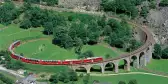 A red train in motion curved along the Brusio Spiral Viaduct on the Bernina Railway