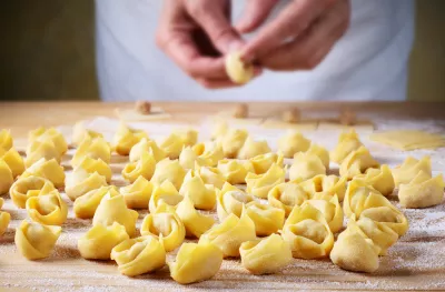 A man making homemade tortellini, on a flour coated wooden table.