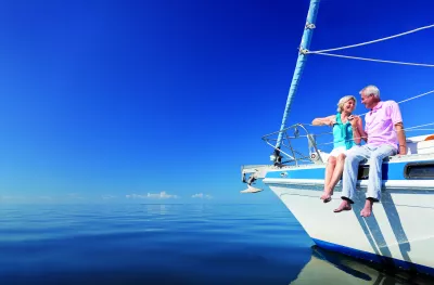 Happy senior couple sitting on the bow of a sail boat on a calm blue sea