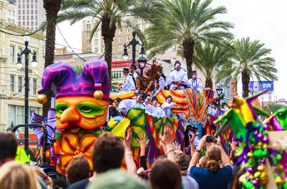 	crowds celebrating Mardi Gras as a float makes its way along the street. men in white and masks throwing beads into the crowds.