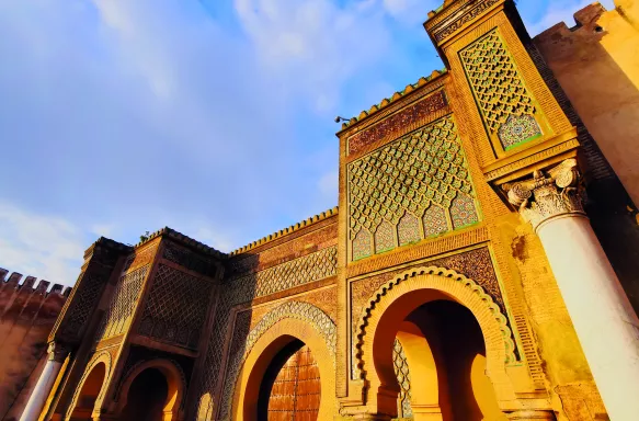 Bab El Mansour Laalej, an ornate monumental gate in the city of Meknes featuring stone archways and lattice-like patterns above stone columns 