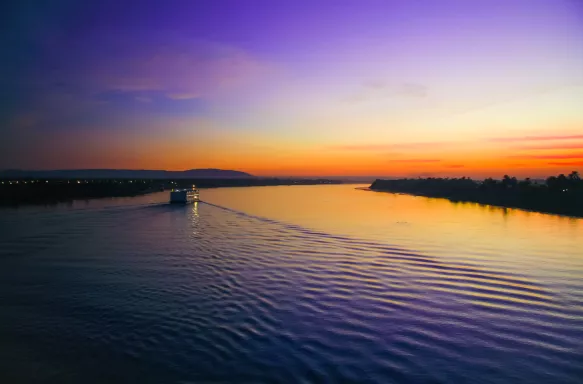 The great Nile River at sunset with a ship in the distance and sun reflections on the water.