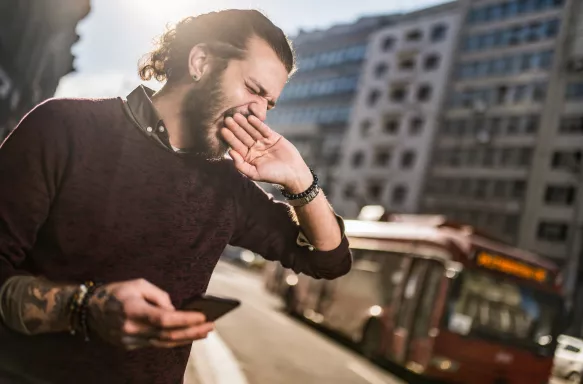 Close-up of a young hipster man yawning as he walks through the city. 