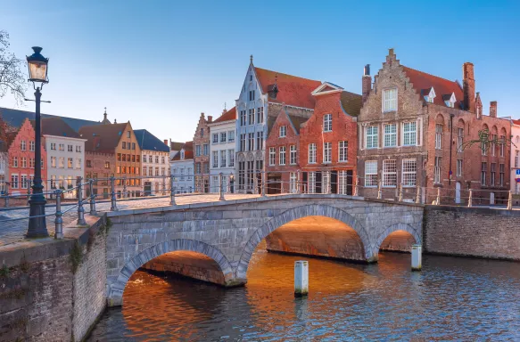 Bruges canal with beautiful medieval coloured houses and sunny bridge during golden hour, Belgium