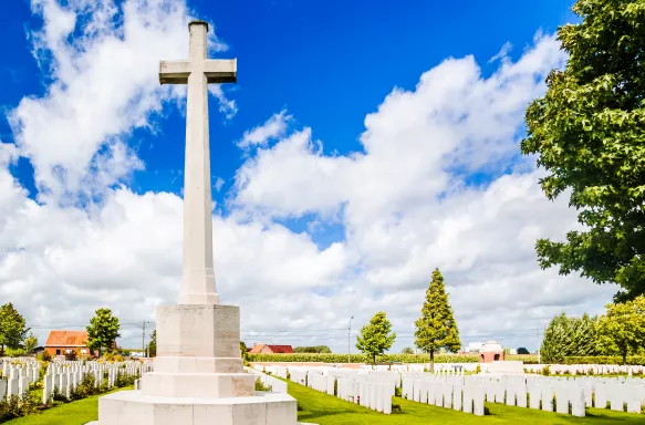 Large white cross headstone in front of rows of grave markers, inside the British cemetery by Ypres, Belgium