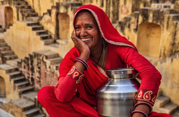 Indian woman in red clothing resting inside stepwell in village near Jaipur, Rajasthan, India.