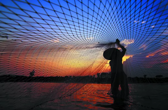 Fisherman casting a net before sunrise along the Mekong River, Thailand.