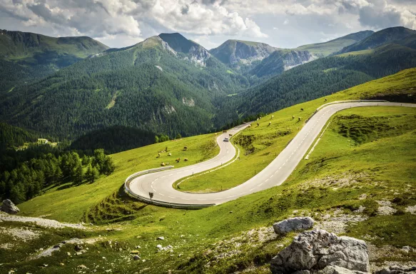 Alpina road at summer-Nockalmstrasse, curving along the natural lines of a green valley, the background showcasing nearby mountain 