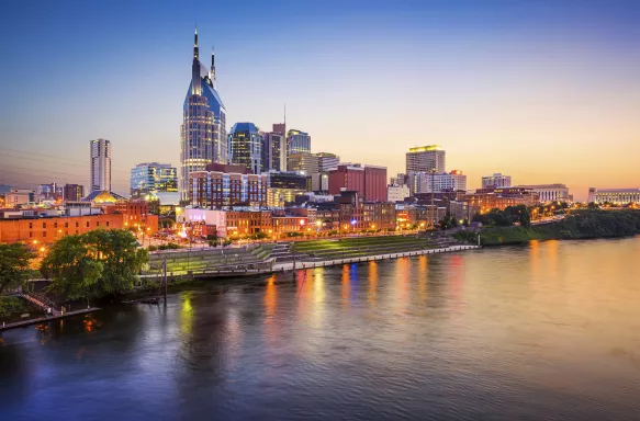 Nashville downtown skyline before sunset along a clear sky, it's reflection displayed in the foreground of the Cumberland River.