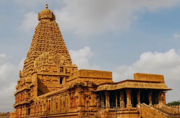 Hindu Temple showcasing Chola architectural style, built with a pyramid shaped spire. Stone steps lead to the entrance hidden under a column-supported roof