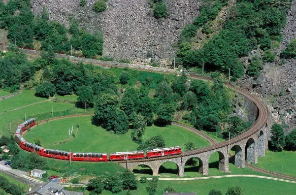 A red train in motion curved along the Brusio Spiral Viaduct on the Bernina Railway