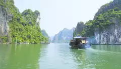 A river boat moving across the turquoise waters of Halong Bay 