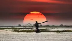 Vietnamese fisherman on his boat during sunset, balancing a oar paddle