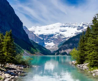 Beautiful Lake Louise with Victoria Glacier in the background and a glistening emerald lake. Several canoes can be seen at a distance on the lake.