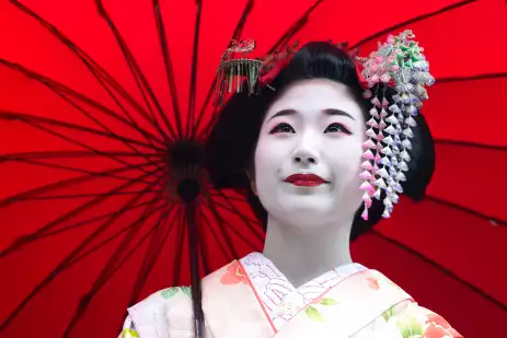 Close-up of a young maiko girl, a geisha in training with a red umbrella, Kyoto 